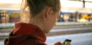 Vrouw kijkt op smartphone op station Leiden. Smartphoneverslaving