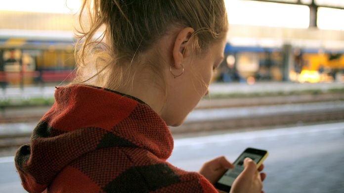 Vrouw kijkt op smartphone op station Leiden. Smartphoneverslaving